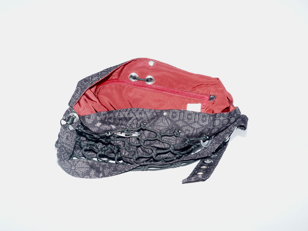 Handmade bag made of upcycled silk kimono and encased in a hand-knotted black paracord. The fabric features purply-black fabric with white stitching and a red interior. The strap includes grommets and a carabiner for adjustability.
